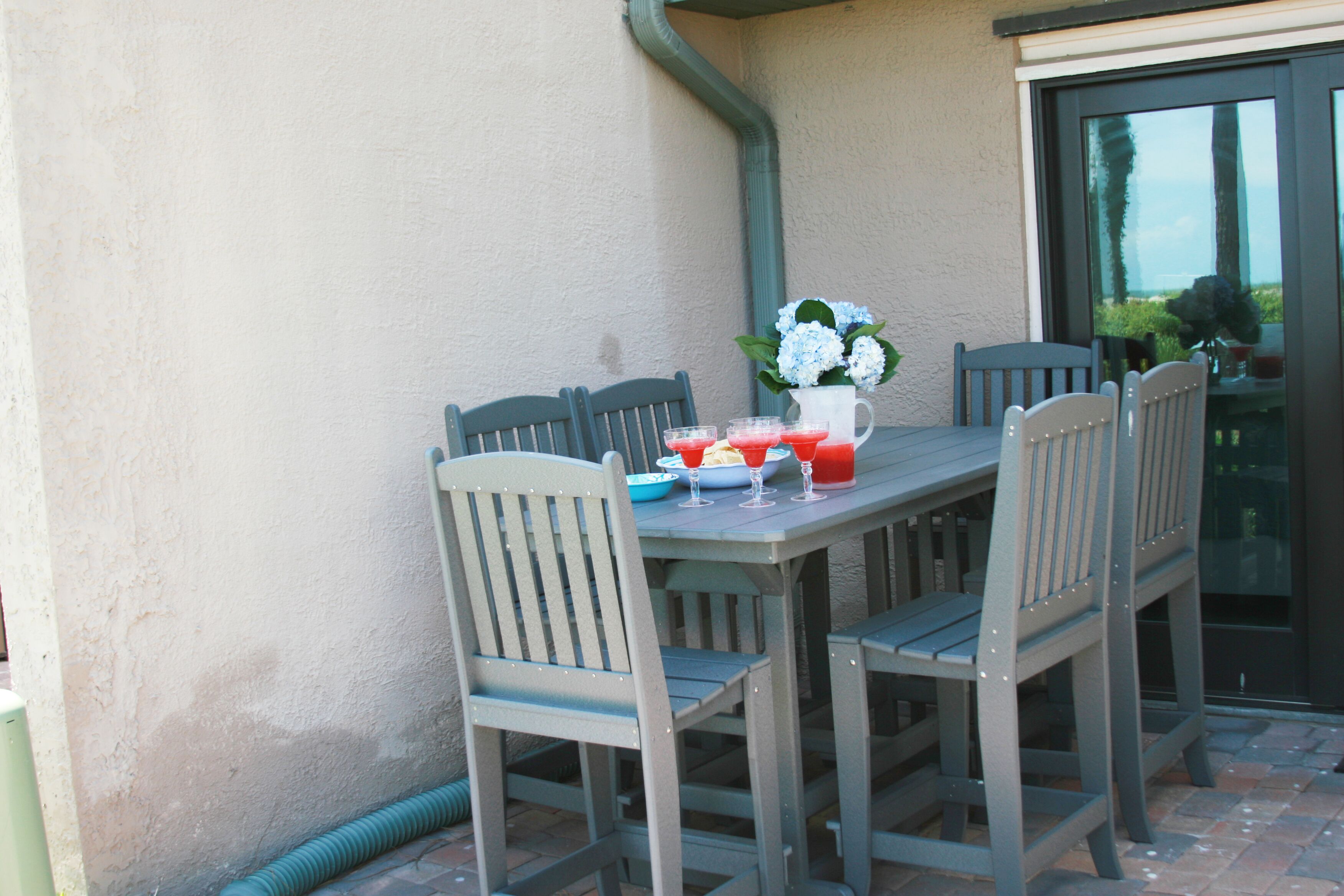 A patio table with four chairs, a pitcher of flowers, and three glasses of red drink.