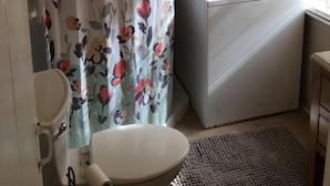 Ett litet badrum med en duschdraperi med blommönster, en vit toalett och en kombinerad tvätt- och torkmaskin.