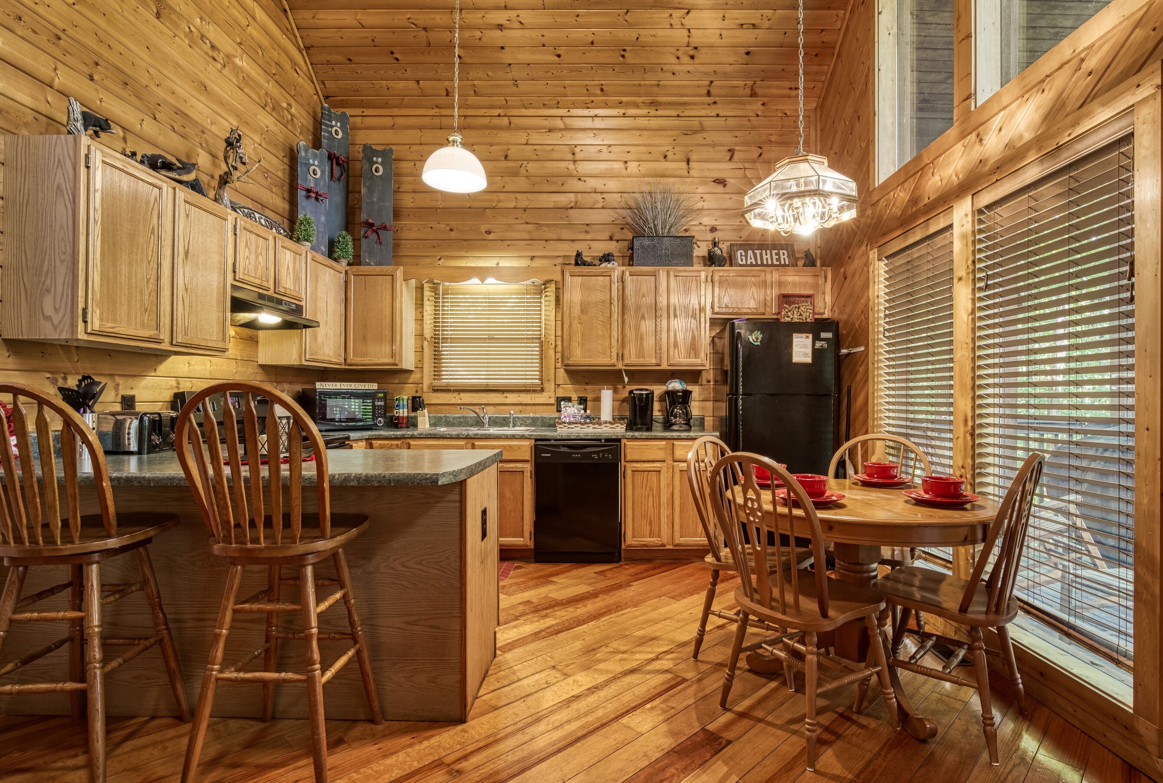 A wooden cabin-style kitchen with wooden cabinets, a central island with bar stools, a dining table with chairs, and a refrigerator.