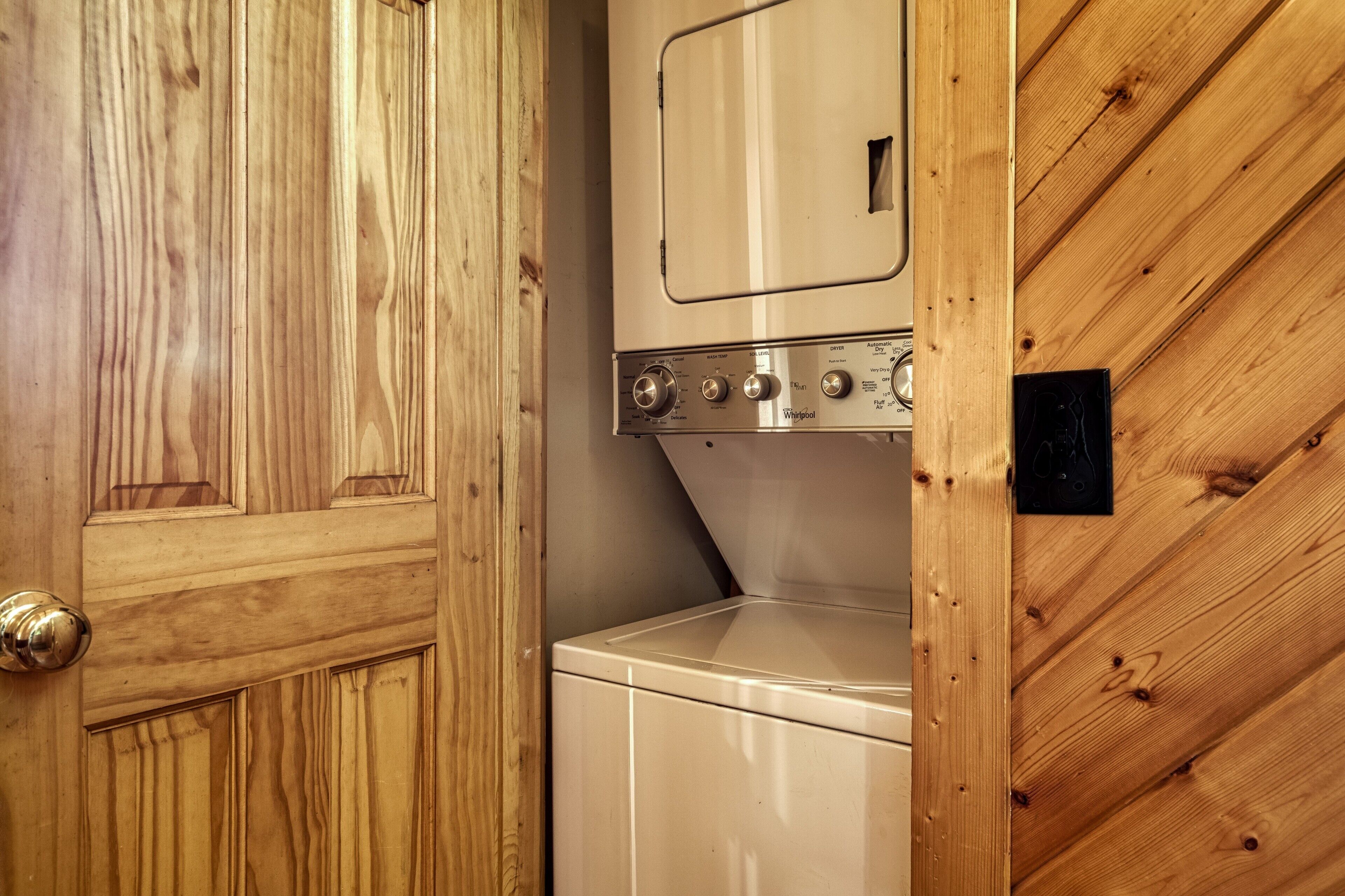 Une buanderie avec un lave-linge et un sèche-linge blancs, des murs en bois et une porte dotée d’une poignée en laiton.