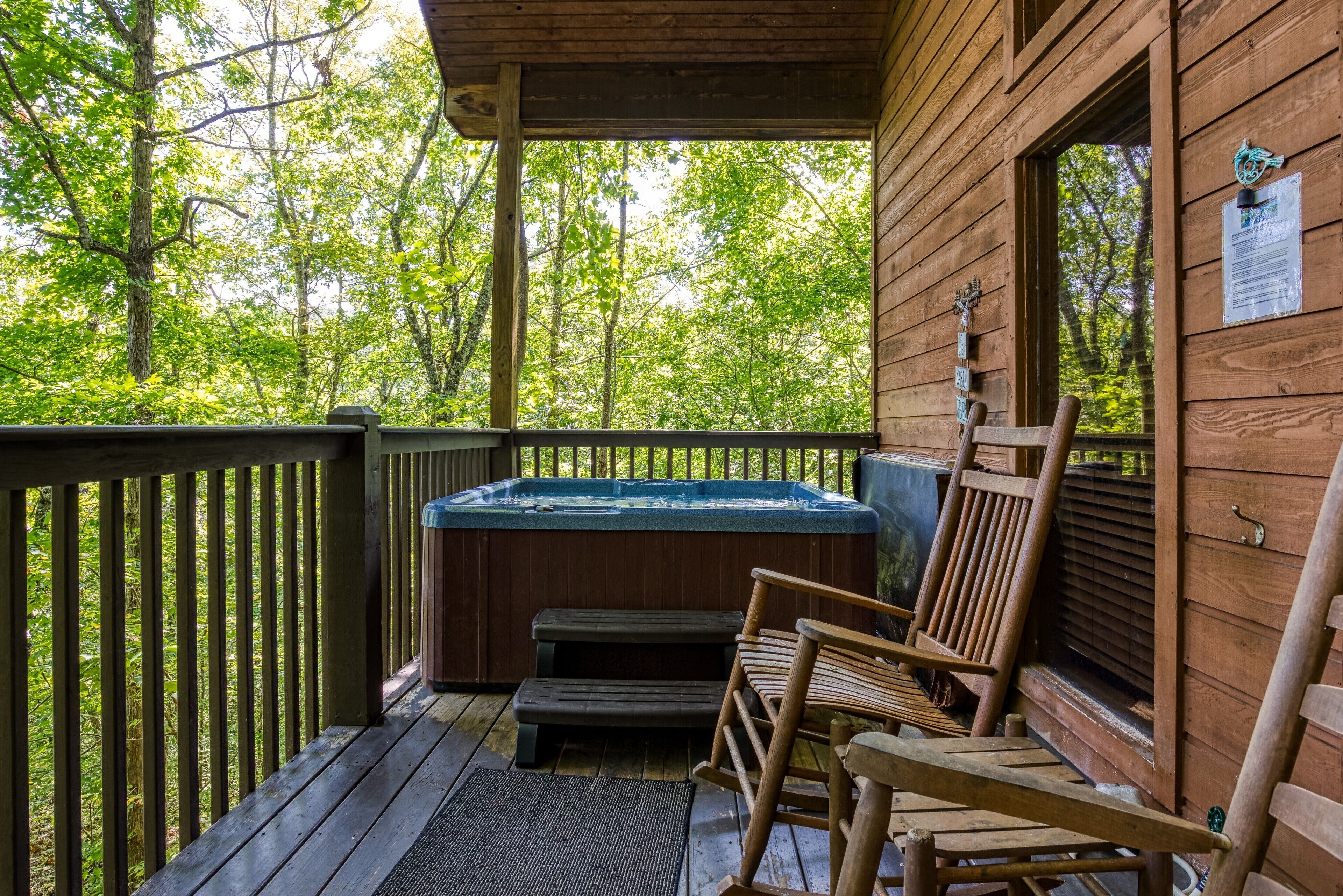 Una cabaña de madera con jacuzzi, terraza de madera y vista al bosque.
