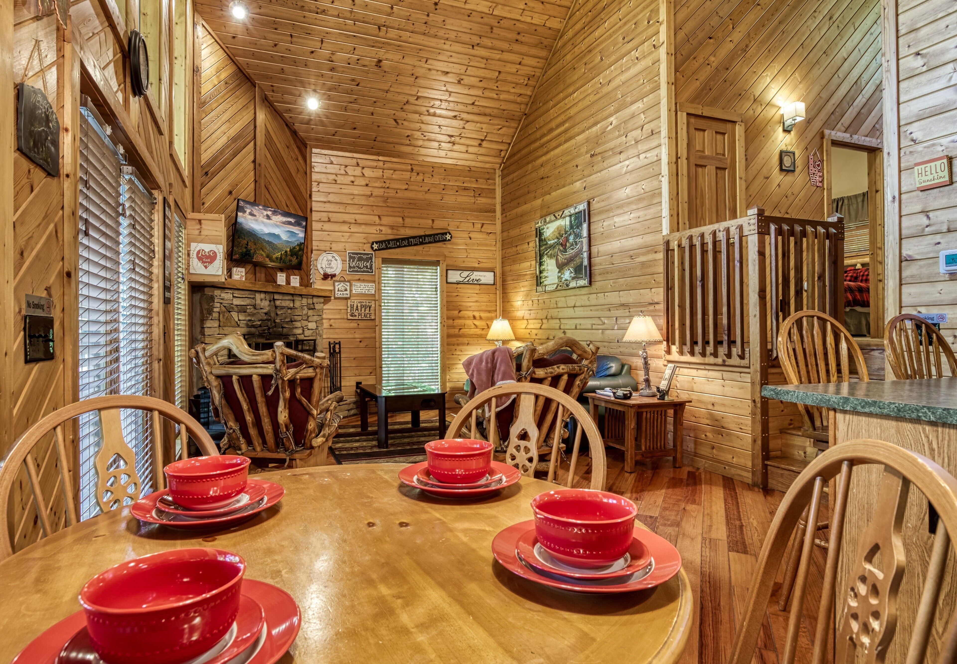 Ein Holzblockhaus-Interieur mit einem Esstisch, gedeckt für vier Personen, Holzstühlen, einem Kamin aus Stein und einer Holzbalkendecke.