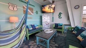 A room with a hammock, two green sofas, a wooden table, a TV, and a refrigerator with magnets. - 🌴 Coco Plum Paradise 🌴 Private Bayfront Home • Pool • Hot Tub • Dock • View (Marathon)