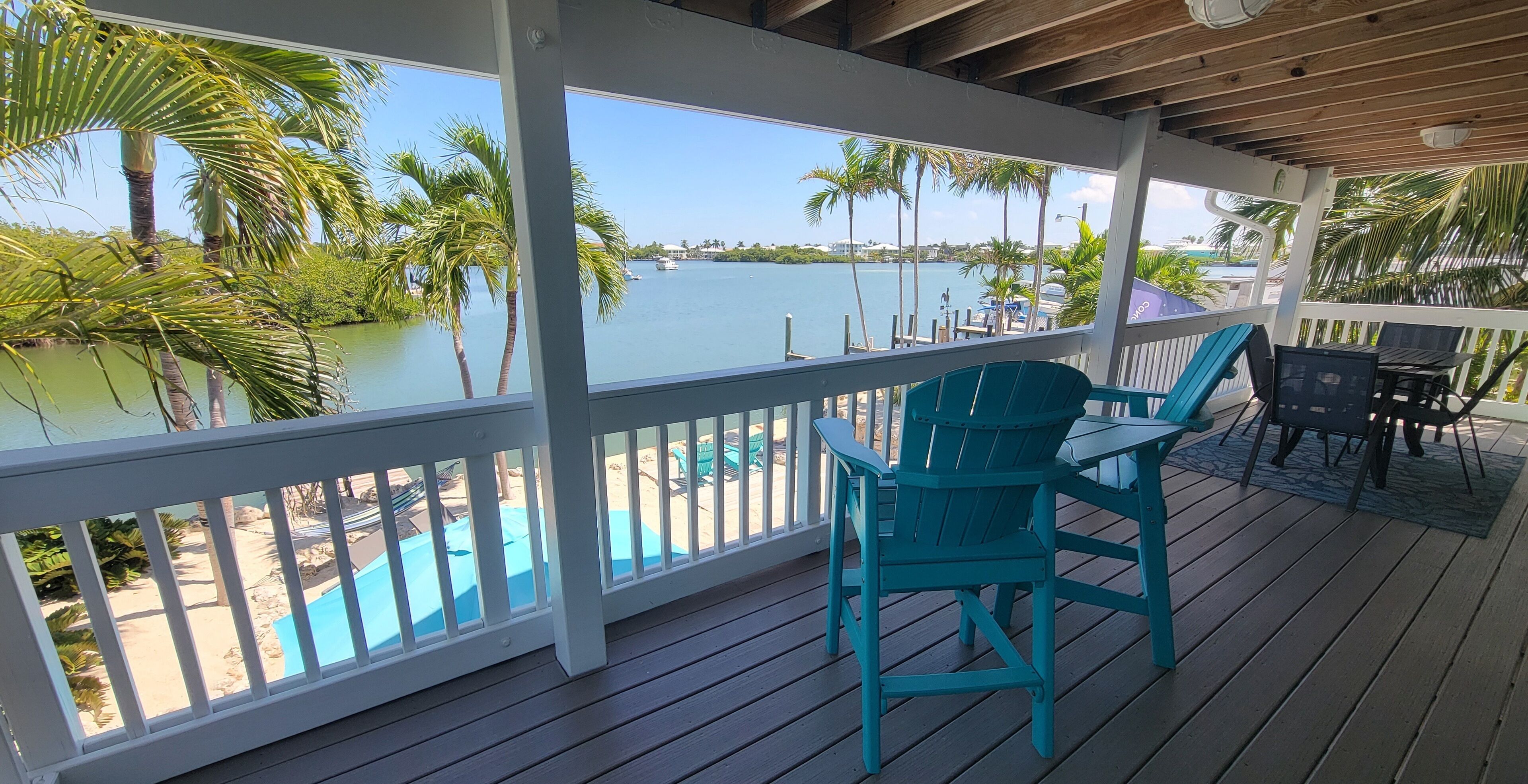 A covered deck with a view of a swimming pool and palm trees.