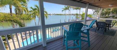 A covered deck with a view of a swimming pool and palm trees.