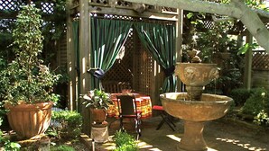 A garden with a wooden pergola, a table with chairs, and a large stone fountain. - Garden Apartment Located in a Wonderful Old Victorian Home (Alameda)