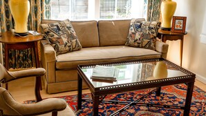 A living room with a beige sofa, patterned cushions, a glass-top coffee table, two lamps, and a patterned rug. - Garden Apartment Located in a Wonderful Old Victorian Home (Alameda)