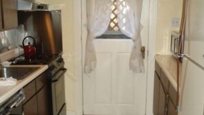 A compact kitchen with wooden cabinets, a stove, and a refrigerator. A patterned rug runs along the floor leading to a door with a decorative window. - Garden Apartment Located in a Wonderful Old Victorian Home (Alameda)