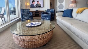 A modern living room with a glass coffee table, a sofa, and a television displaying two people. - 14th FL, 2312 Sq Ft, Luxury Gulf Front,  corner 3BR/4BA, plus bonus den, amazing (Pensacola)