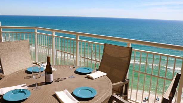 A round table with blue plates, a wine bottle, and glasses set for two, overlooking a beach with the ocean. - 14th FL, 2312 Sq Ft, Luxury Gulf Front,  corner 3BR/4BA, plus bonus den, amazing (Pensacola)