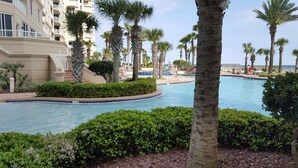 A pool area with palm trees, a building with balconies, and a clear blue sky. - 14th FL, 2312 Sq Ft, Luxury Gulf Front,  corner 3BR/4BA, plus bonus den, amazing (Pensacola)