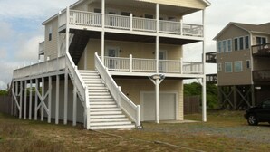 A two-story building with a balcony on the upper floor, a staircase leading to the entrance, and a garage. - Amazing Ocean & Bay Views Beach access is feet away Heated Pool Hot Tub Tiki Bar (North Topsail Beach)