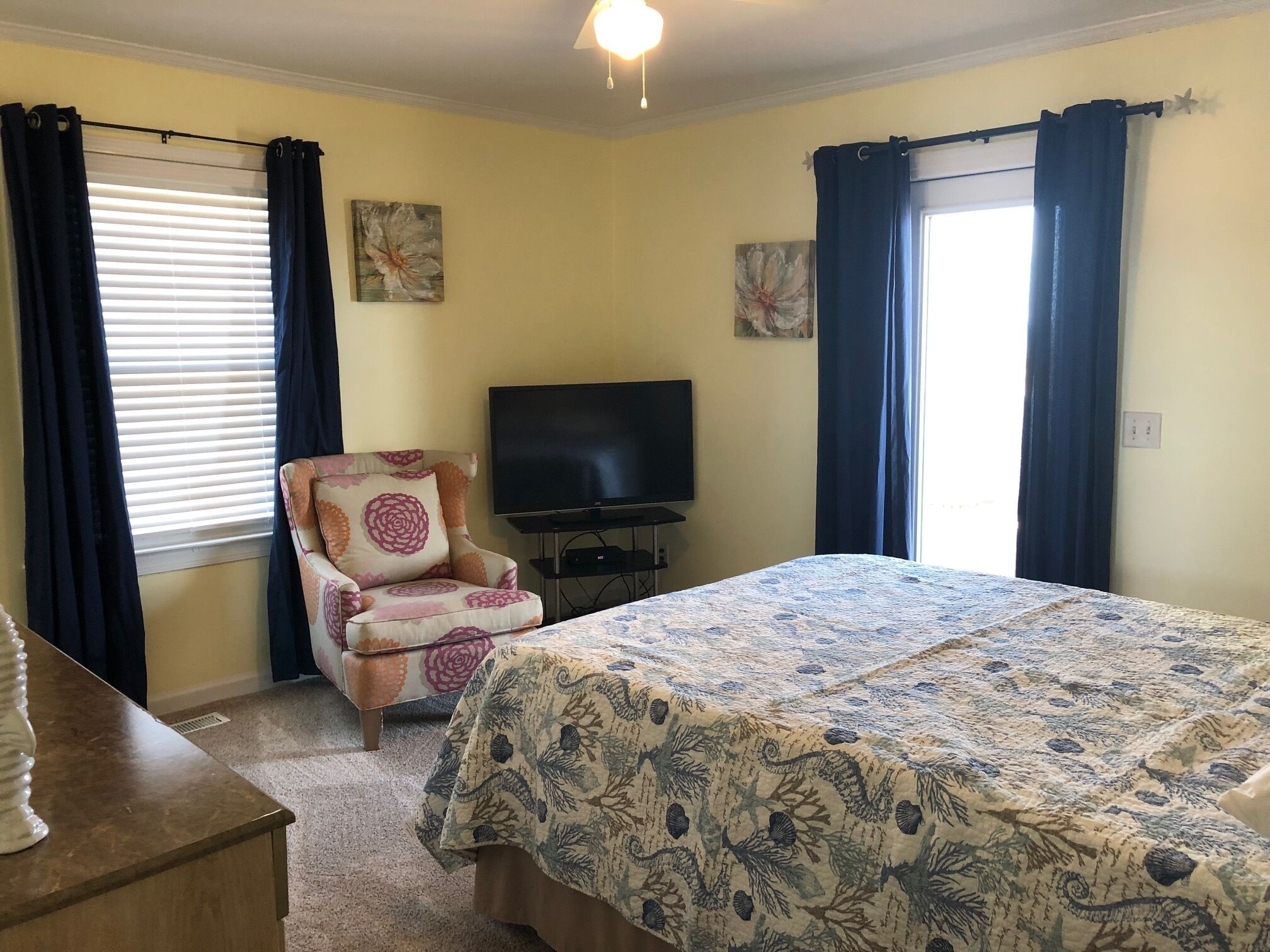 Un dormitorio con cama, una silla, televisor y cortinas.