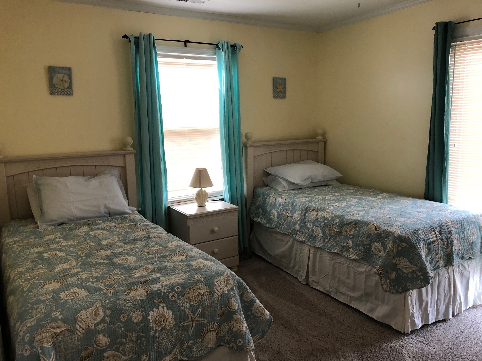 A room with two single beds, a nightstand with a lamp, and a window with curtains.