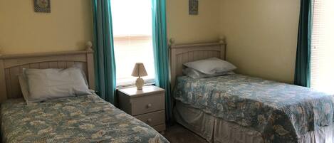 A room with two single beds, a nightstand with a lamp, and a window with curtains.