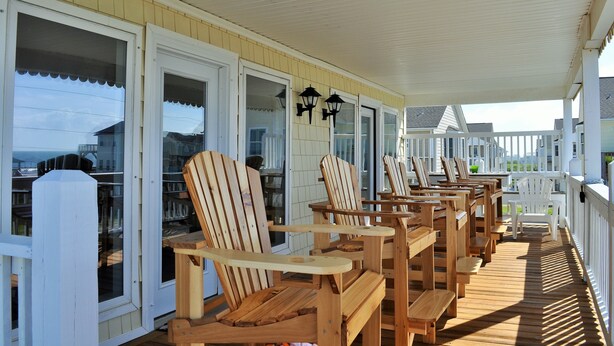 A covered outdoor seating area with wooden Adirondack chairs and tables, white railings, and a view of the ocean. - Amazing Ocean & Bay Views Beach access is feet away Heated Pool Hot Tub Tiki Bar (North Topsail Beach)