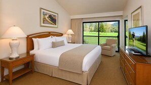 A hotel room with a large bed, two bedside lamps, a television, a chair, a wooden dresser, and a balcony with a view of a golf course.