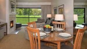 A dining area with a round table, chairs, a bowl of fruit, and a bottle of wine.