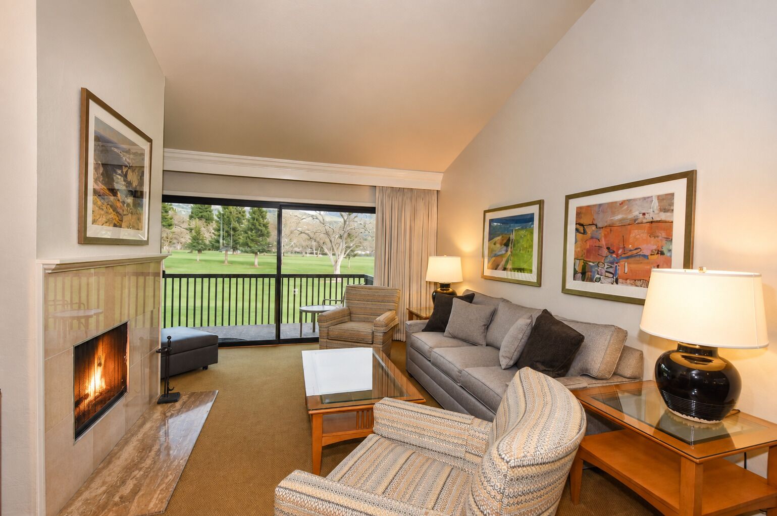 A living room with a fireplace, a sofa, a chair, a coffee table, and a lamp. There are two framed pictures on the wall.