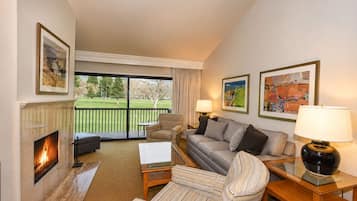 A living room with a fireplace, a sofa, a chair, a coffee table, and a lamp. There are two framed pictures on the wall.