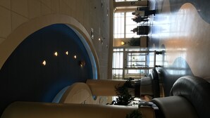 Eine moderne Lobby mit einem großzügigen, geschwungenen Sitzbereich, einem Empfangstresen und großen Fenstern, die viel Tageslicht hereinlassen.