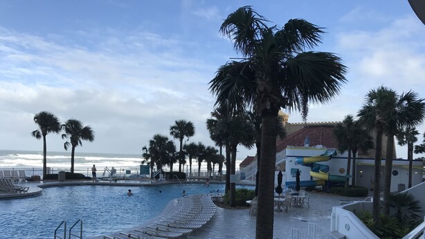 Ein Poolbereich mit Palmen, einer Rutsche und Blick auf den Ozean.
