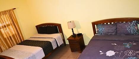 A room with two wooden beds, a nightstand with a lamp, and a curtain.