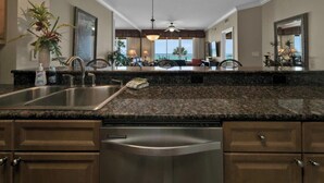 A kitchen with granite countertops, stainless steel appliances, and a view of the ocean through large windows.