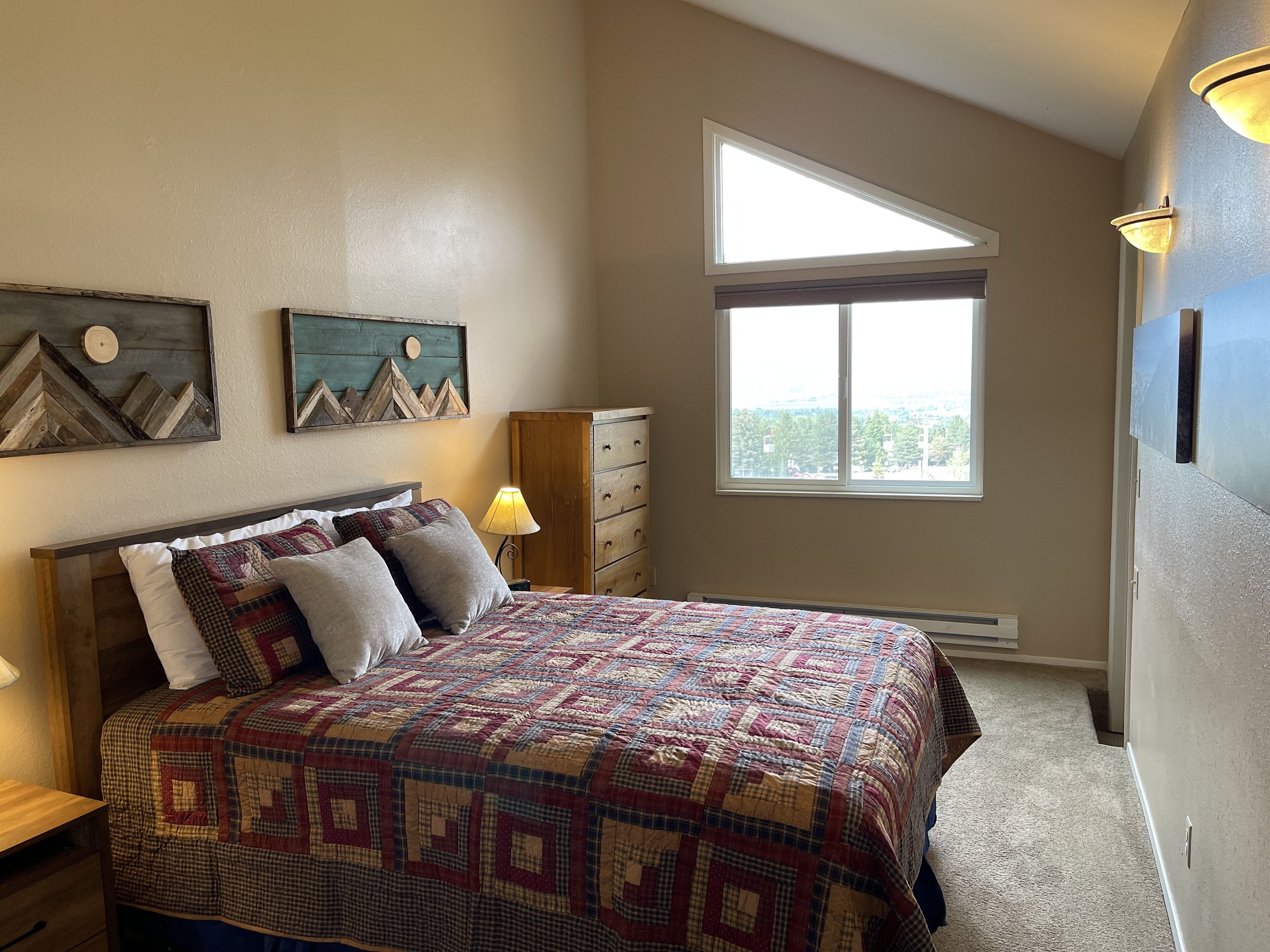 A bedroom with a large bed, a dresser, a window with a view, and wall art.