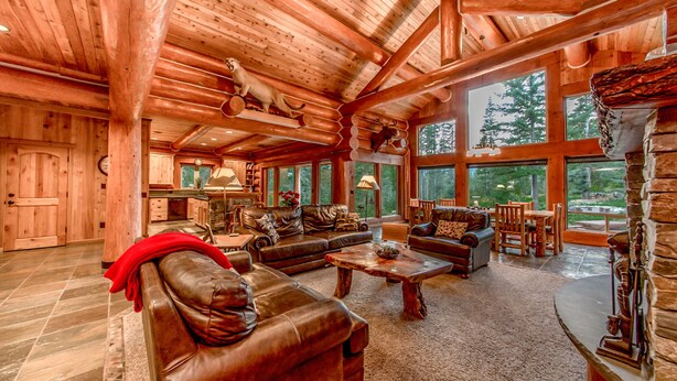 A spacious log cabin interior with a large living area, leather furniture, and large windows offering views of the forest. - Crest Lodge - 3,700sf Log Home with 5 bedrooms + Sleeps 15-17 (Ronald)