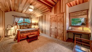 A cozy bedroom with a wooden ceiling, a bed, a desk, and a large window. - Crest Lodge - 3,700sf Log Home with 5 bedrooms + Sleeps 15-17 (Ronald)