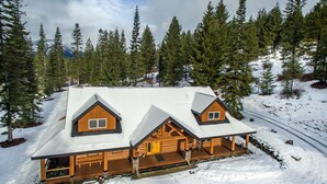 A log cabin with a snow-covered roof, wooden exterior, and a porch with outdoor seating. - Crest Lodge - 3,700sf Log Home with 5 bedrooms + Sleeps 15-17 (Ronald)