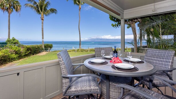 A covered outdoor dining area with a view of the ocean and palm trees.