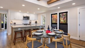 A modern kitchen with white cabinets, a central island, and a dining area with a glass table and wooden chairs.
