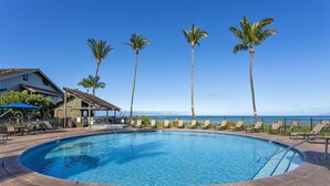 A circular pool with lounge chairs and palm trees, overlooking a beach.