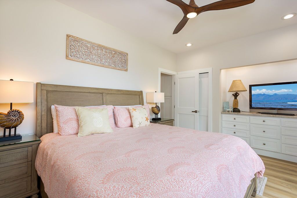 A bedroom with a large bed, a ceiling fan, a television, and a decorative wall piece.