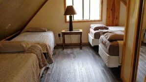 A cozy attic bedroom with two beds, a small table, and a window. - The smaller version to the Restin' at Weston (weston)