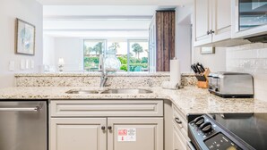 A modern kitchen with granite countertops, stainless steel appliances, and a large window offering a view of greenery. - Oceanfront King & Prince Villa | Breathtaking Ocean Views | Access to Resort Amenities! (St. Simons Island)
