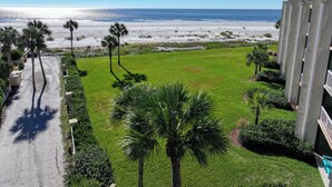 A view of a beach with palm trees and a building with a balcony. - Oceanfront King & Prince Villa | Breathtaking Ocean Views | Access to Resort Amenities! (St. Simons Island)