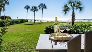A table with a bottle and two glasses on a tray, overlooking a beach with palm trees. - Oceanfront King & Prince Villa | Breathtaking Ocean Views | Access to Resort Amenities! (St. Simons Island)