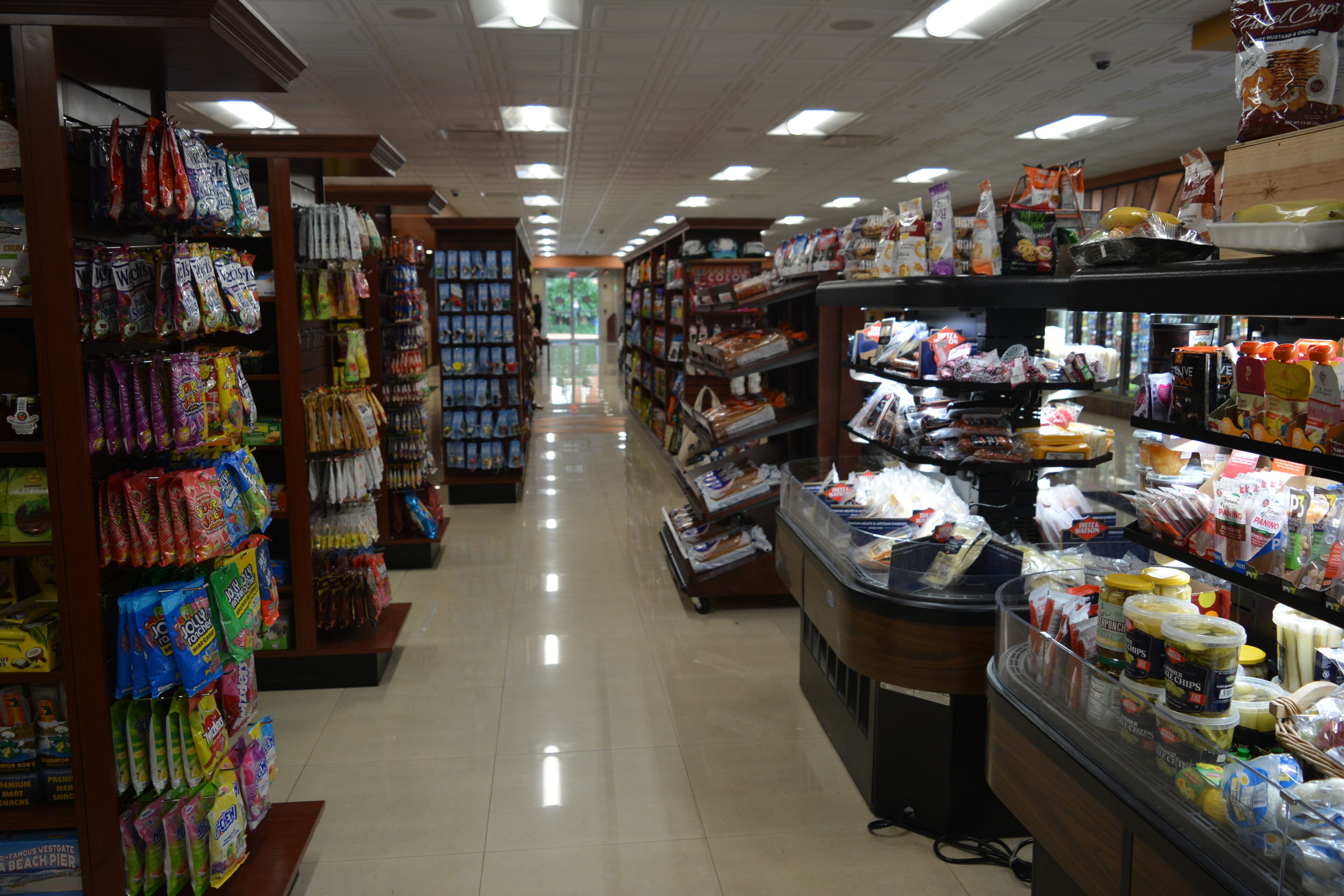 Un pasillo de un supermercado con estantes llenos de bocadillos, bebidas y artículos para el hogar.