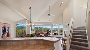 Un amplio espacio de sala con un gran ventanal, un ventilador de techo y una escalera.