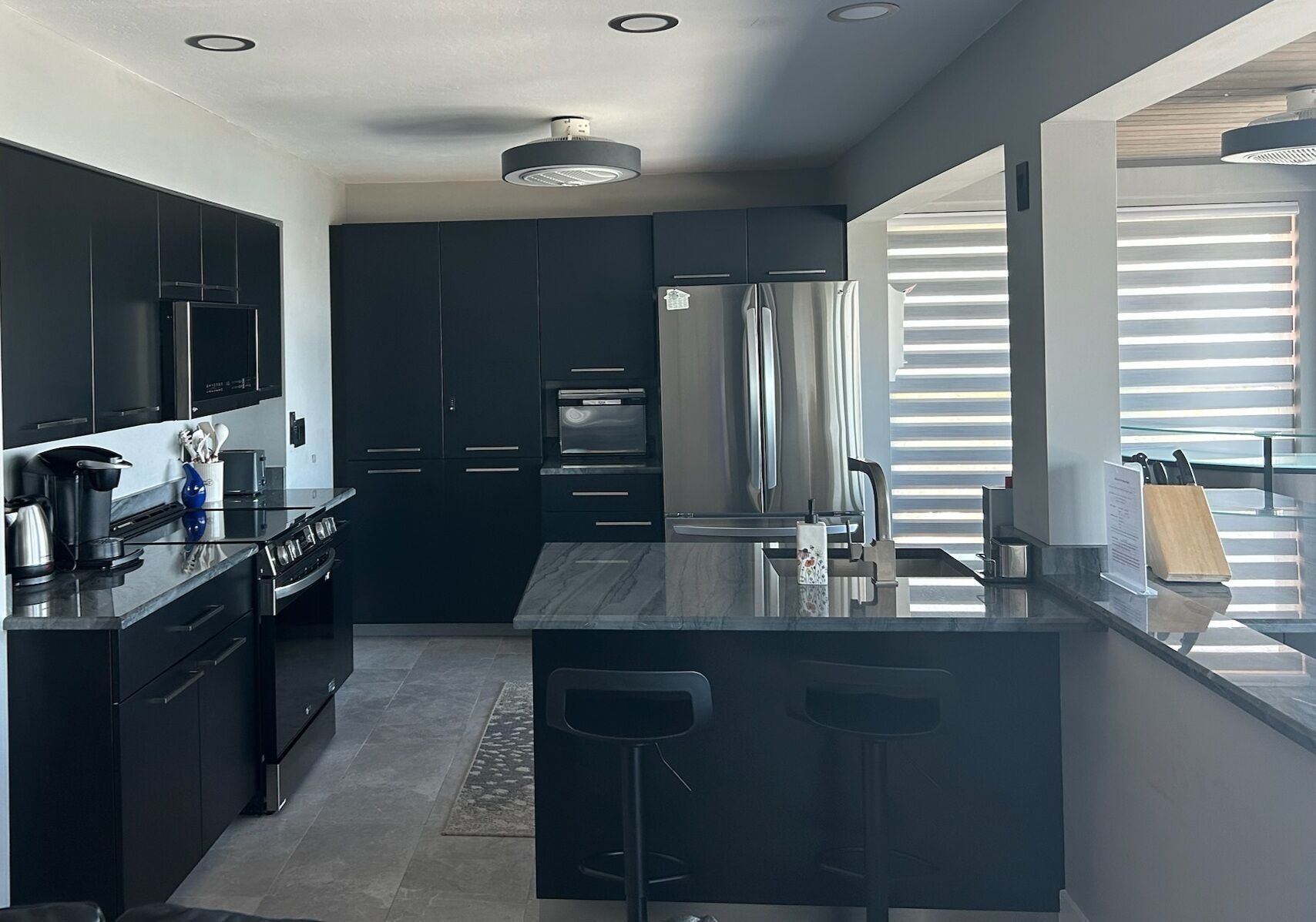 A modern kitchen with dark cabinetry, stainless steel appliances, and a central island with bar stools.