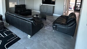 Een moderne woonkamer met een modulaire bank, een zwarte fauteuil en een aan de muur bevestigde televisie.