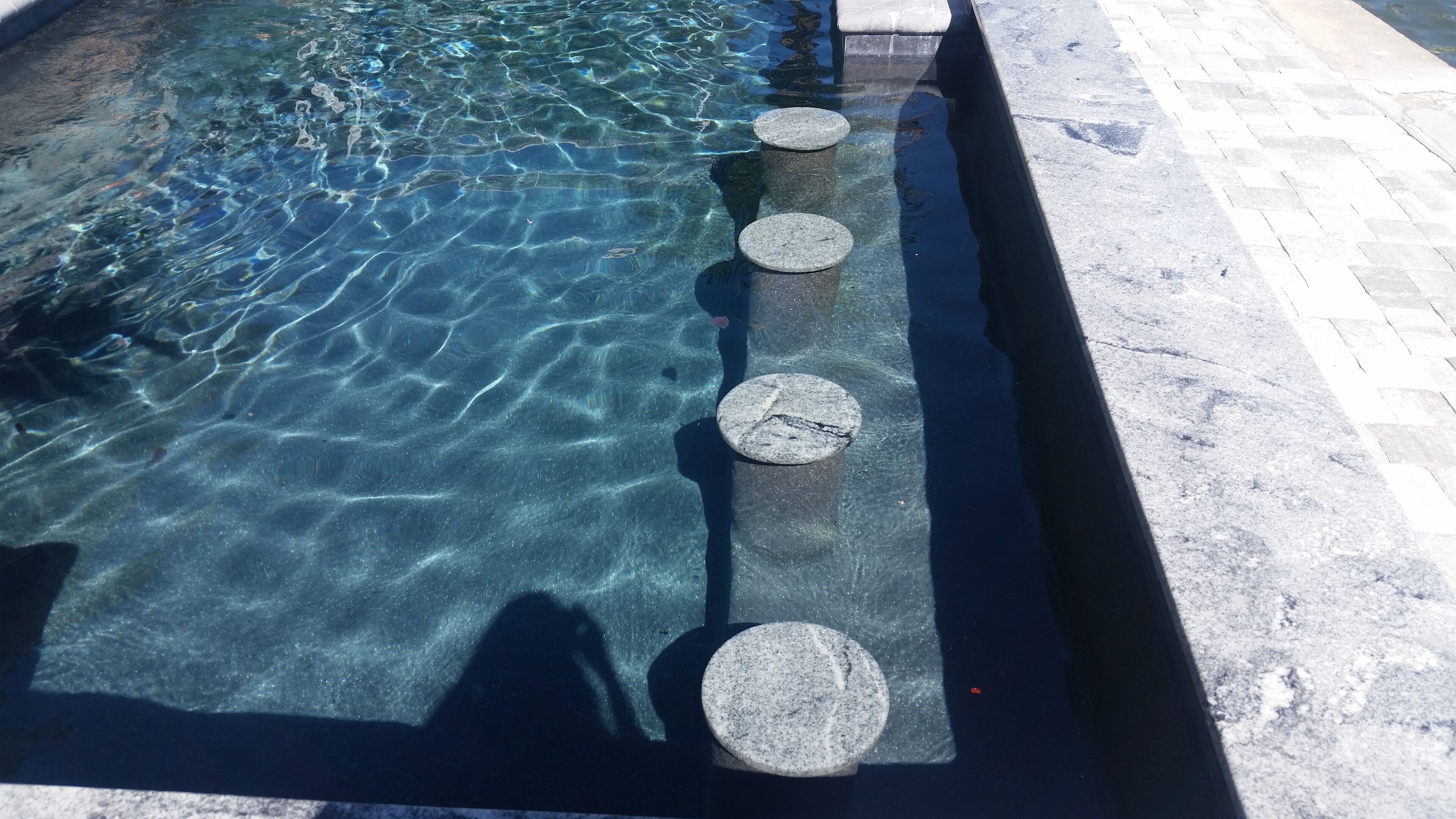 Una piscina cristalina con cuatro escalones circulares de piedra que bajan al agua.