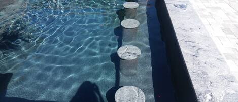 Una piscina cristalina con cuatro escalones circulares de piedra que bajan al agua.