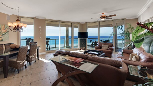 Ein geräumiges Wohnzimmer mit einem großen Fenster zur Terrasse, von der aus man den Blick aufs Meer hat. Es gibt einen Essbereich mit Korbmöbeln und ein Fernseher in der Mitte des Raumes.