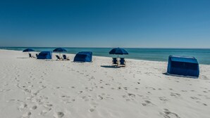 Ein Strand mit mehreren blauen Sonnenschirmen und Liegestühlen.