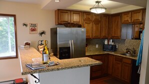A kitchen with wooden cabinets, a stainless steel refrigerator, granite countertops, and a small island with a wine bottle and glasses.