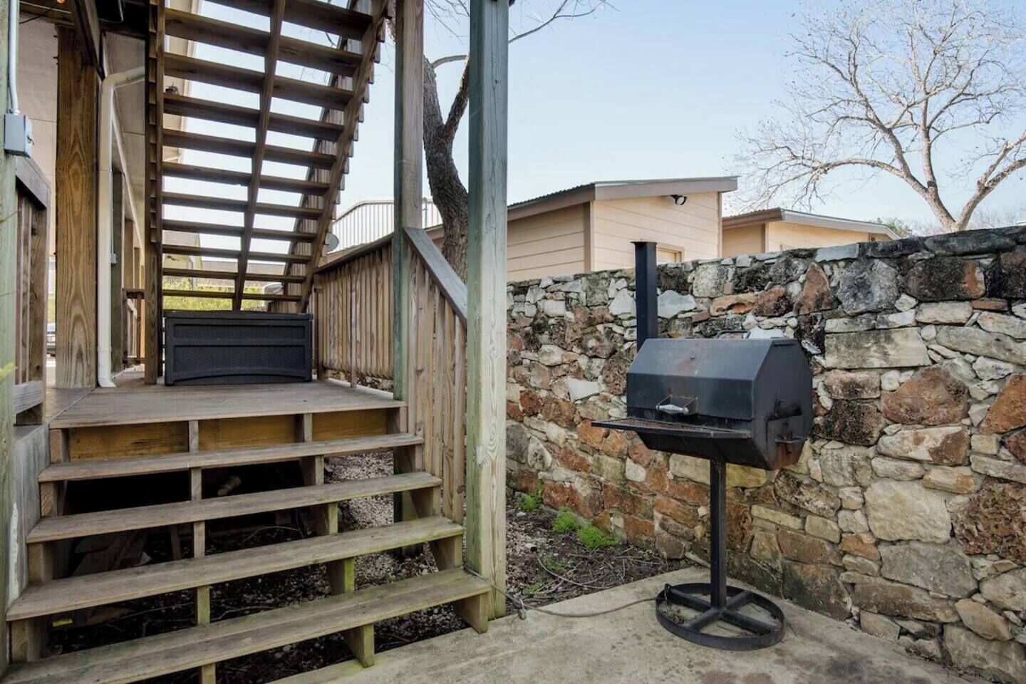 Une terrasse en bois avec un muret en pierre et un barbecue.